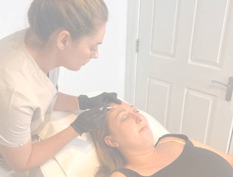 Assured Aesthetics aesthetician performing a facial treatment on a female client lying down.
