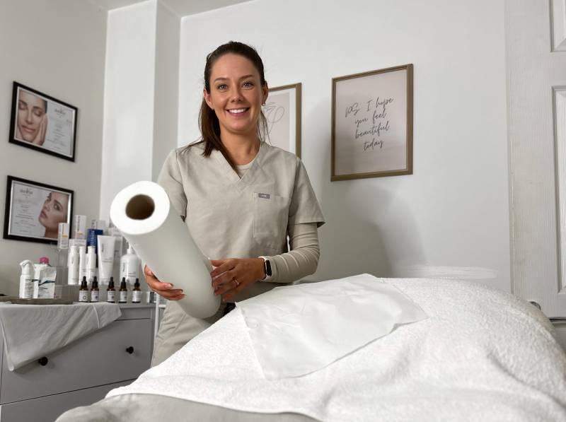 A smiling female beautician holding a roll of paper in a spa room.