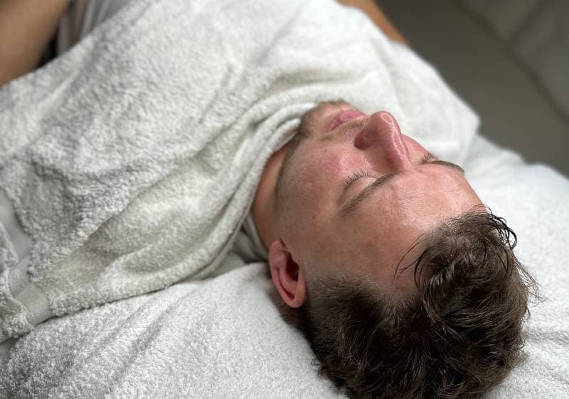 A man lying down with a white towel covering his body, resting peacefully after a Chemical Peel treatment.